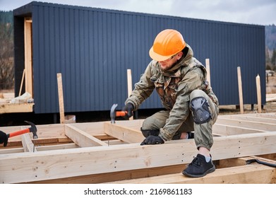Man worker building wooden frame house on pile foundation. Carpenter hammering nail into wooden joist, using hammer. Carpentry concept. - Shutterstock ID 2169861183