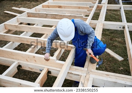 Man worker building wooden frame house on pile foundation. Carpenter hammering nail into wooden plank, using hammer. Carpentry concept.