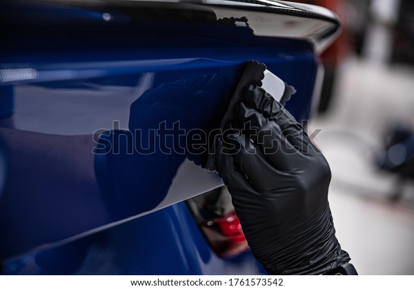 Man worker of car detailing\
studio applying ceramic coating on car paint with sponge\
applicator.