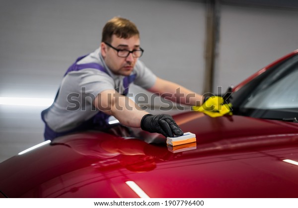 Man worker of car detailing\
studio applying ceramic coating on car paint with sponge\
applicator