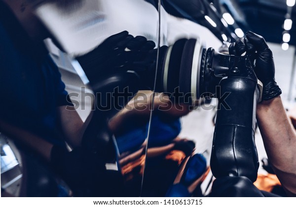 Man worker in car wash polishing car with\
electric polisher. Car\
detailing