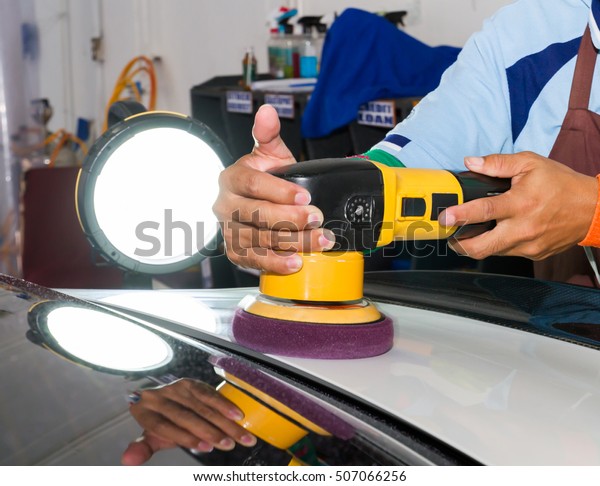 Man\
worker coating white car with wax and tool in\
garage.
