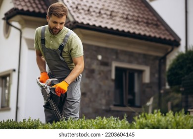 Man Worker Cutting Bushes With An Electric Saw In The Yard