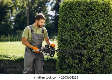 Man Worker Cutting Bushes With An Electric Saw In The Yard