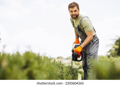 Man Worker Cutting Bushes With An Electric Saw In The Yard