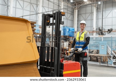 Man worker driver using forklift electric or electric pallet stacker lift moving cardboard boxes sheet goods in paper box factory. Male warehouse worker working in store warehouse.
