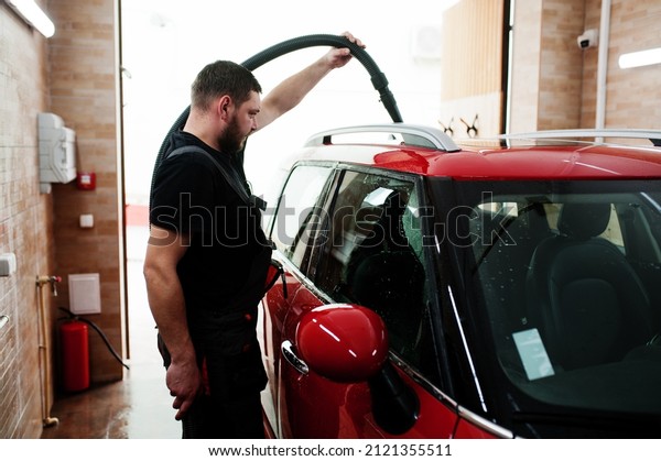 Man worker drying red car in detailing garage\
after washing.