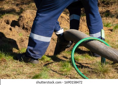 Man worker holding pipe, providing sewer cleaning service outdoor. Sewage pumping machine is unclogging blocked manhole