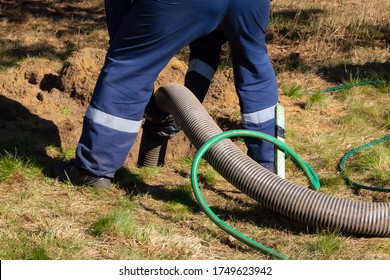 Man worker holding pipe, providing sewer cleaning service outdoor. Sewage pumping machine is unclogging blocked manhole