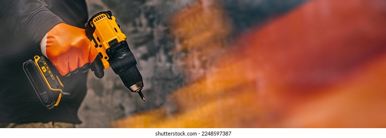 Man worker holds an electric screwdriver in his hands close-up against the background of a construction tool and a concrete wall. Long banner with glow effects - Powered by Shutterstock