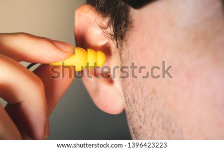 Man worker inserting yellow hearing safety protection earplug in his ear close-up view