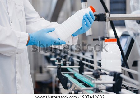 Man worker operator inspecting milk bottles production line dairy factory industry, automatic conveyor for transporting.