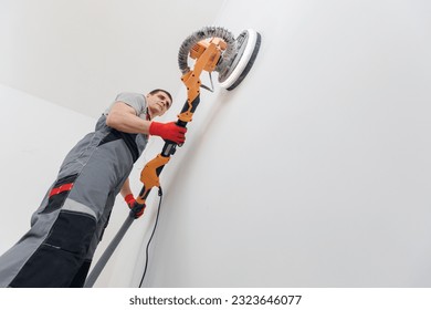 Man worker Painter work with white wall polishing and sanding surface after putty for painting in new apartment.