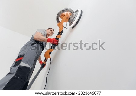 Man worker Painter work with white wall polishing and sanding surface after putty for painting in new apartment.
