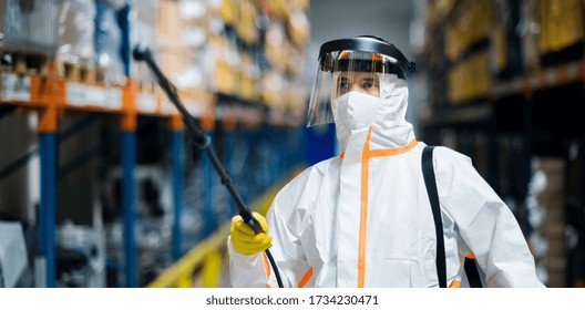 Man Worker With Protective Mask And Suit Disinfecting Industrial Factory With Spray Gun.