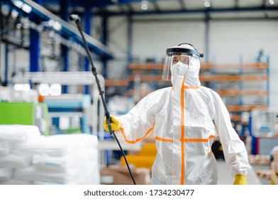 Man worker with protective mask and suit disinfecting industrial factory with spray gun.