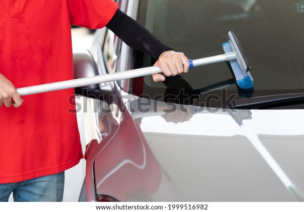 Man worker in red uniform using sponge \
clean windscreen and checking wiper blade of car while representing\
high quality service of gas fuel\
station