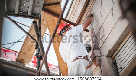 Man worker standing on scaffolding, perform work on the restoration of the facade of the old building. Repairing and renovate
