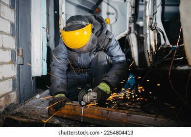 man worker in a uniform and a mask works with a grinder, cuts metal for a truck body repair. - Shutterstock ID 2254804413