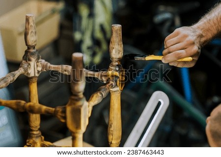 A man, a worker, varnishes furniture with a brush, painting a wooden chair with varnish in the workshop. Photography, handcraft work concept.