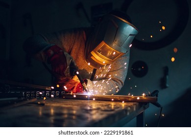 Man worker working with a metal product and welding it with a arc welding machine in a workshop. Industrial manufacturing. Welding metal part in a factory. Orange sparks. Copy space. - Shutterstock ID 2229191861