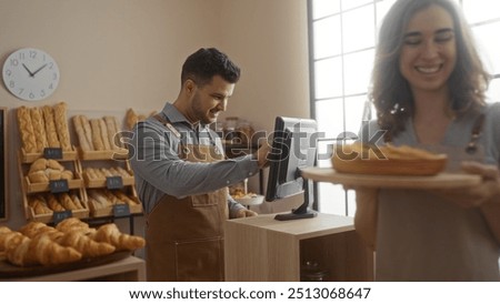 Man working at a bakery counter while a woman carries fresh bread in a warmly lit, modern bakery interior filled with an assortment of breads and pastries