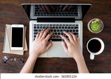 A man is working by using a laptop computer on vintage wooden table. Hands typing on a keyboard. Top view. - Shutterstock ID 363301124