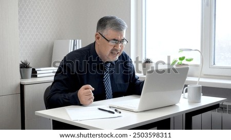 A man working at a computer in despair. He clenches his fists and looks at the monitor screen with anger. Perfect for content about remote work, freelancing and office work.