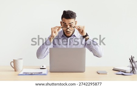 Man Working at Desk With Laptop While Adjusting Glasses and Appearing Surprised at Something