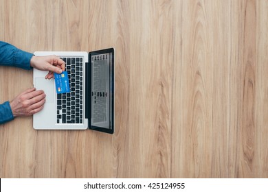 Man working at desk and purchasing products online, he is making a payment using a credit card, online shopping concept