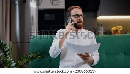Man working with documents at remote workplace. Business man talking mobile phone and revisioning financial documents at home.