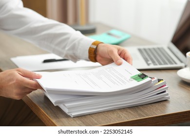 Man working with documents at wooden table in office, closeup