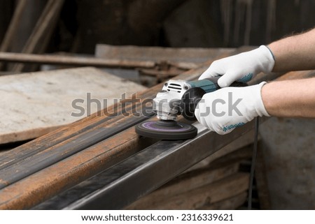 A man working with electric angle grinder tool. Removing rust a metal square tube. Hands in white gloves hold a power tool, wire brush.