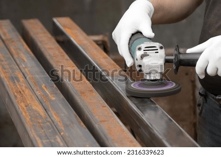 A man working with electric angle grinder tool. Removing rust a metal square tube. Hands in white gloves hold a power tool, wire brush.