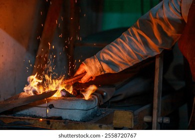 A man is working with a forge, using a hammer to shape metal. The forge is hot and the man is wearing a leather apron. The scene is intense and focused - Powered by Shutterstock