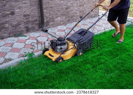 The man is working in the garden. Mowing grass with a lawn mower.                            