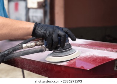 A man working with grinding tool. Sanding of car elements. Garage painting of cars. Cleans car elements from paint. Hands in black gloves hold a power tool. Close up. - Powered by Shutterstock