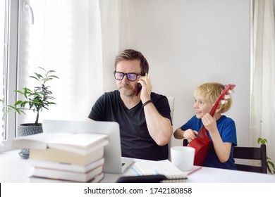 Man Working From Home With Laptop During Quarantine. Home Office And Parenthood At Same Time. Exhausted Parent With Hyperactive Child. Chaos With Kids During Isolation