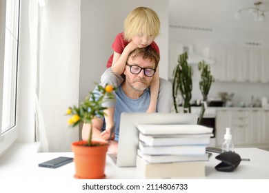 Man is working from home with laptop during quarantine. Home office and parenthood at same time. Exhausted parent with hyperactive child. Chaos with kids during isolation - Shutterstock ID 2114806733