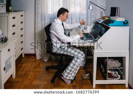 Man working from home with laptop wearing shirt, tie and pajama pants