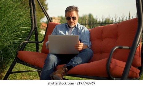 Man Working At Home Office, Sitting In Swinging Couch, Using Laptop Computer. Thinking, Relaxing. Slow Motion Video.