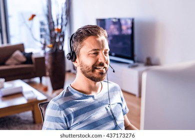 Man Working From Home On Computer, Wearing Headset