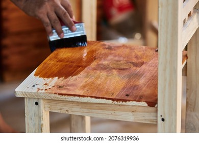 Man Working At Home Varnishing A Wooden Chair With A Brush And Varnish. Man Composing His Chair Himself.