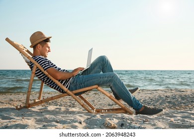 Man Working With Laptop In Deck Chair On Beach