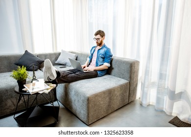 Man working with laptop on the couch at the bright living room of the modern apartment - Shutterstock ID 1325623358