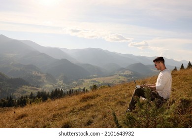 Man Working With Laptop Outdoors Surrounded By Beautiful Nature. Space For Text