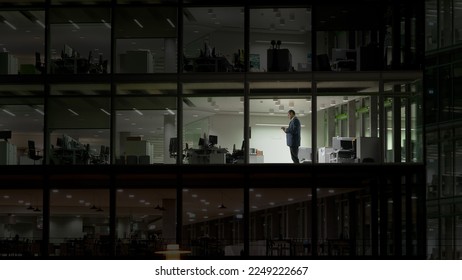 Man working late night in empty building with transparent glass window, modern - Powered by Shutterstock