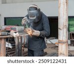 Man is working at metal factory, he is welding a edge of boiler frame in factory.