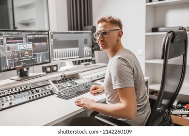 Man working in music studio using computer wearing glasses. Sound engineer working and mixing track. Programmer watching at display of it while listening music. Technology concept