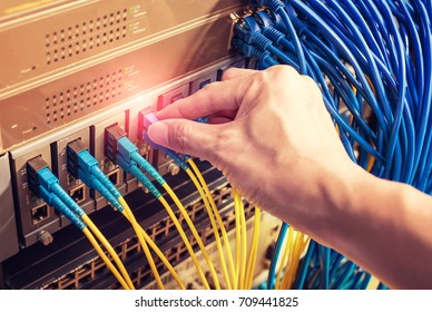 man working in network server room with Fiber Optic cables connected to optic ports and UTP - Powered by Shutterstock